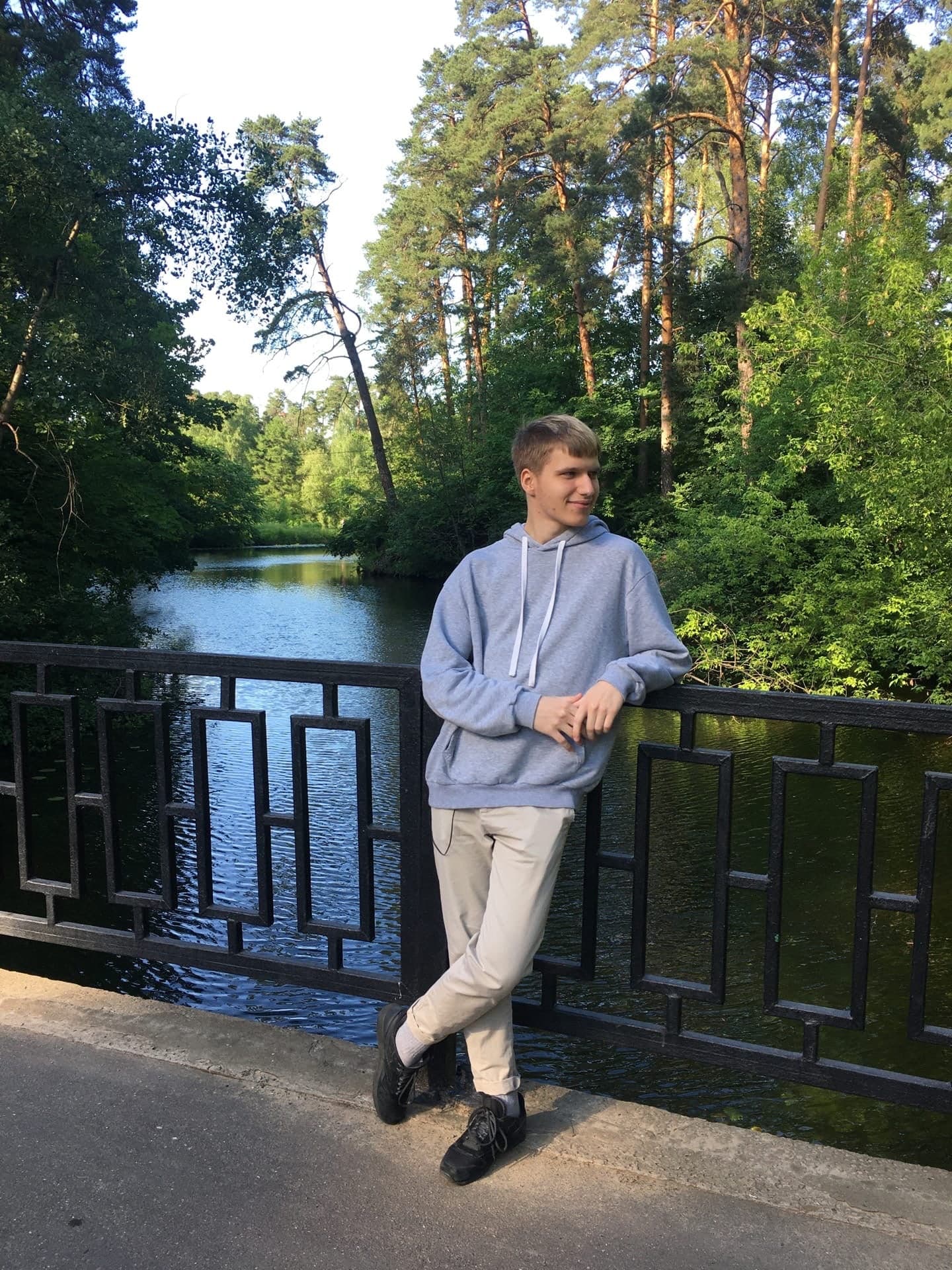 Степан на мосту у реки, в сером худи